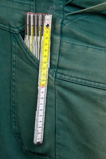 A folding rule made of wood is in the pocket of a pair of green work trousers.