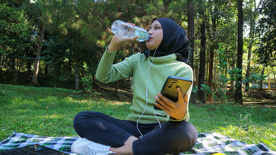 istock Happy muslim woman listen music on mobile phone at park while drinking mineral water, free space 1646588247
