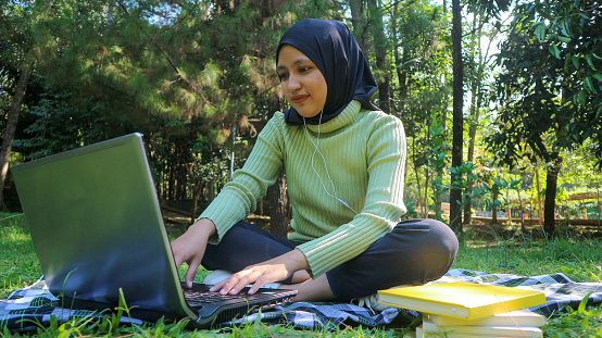 Asian girl muslim student using laptop at park, resting and studying outdoors, free space