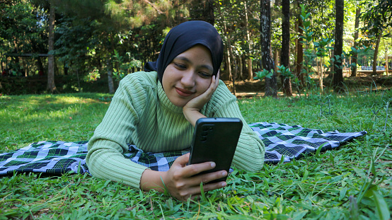 Happy muslim woman having video call on mobile phone at park, using headset, free space