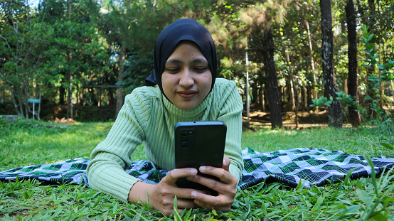 Happy muslim woman having video call on mobile phone at park, using headset, free space
