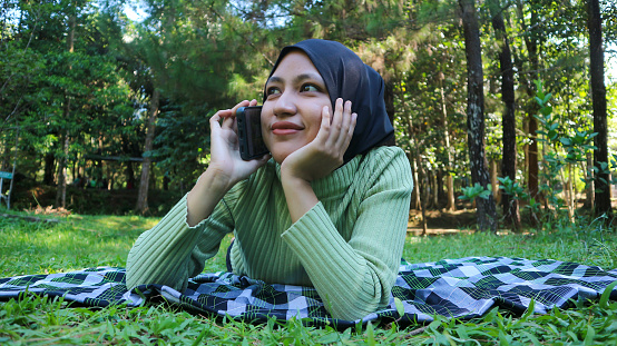 Happy muslim woman having video call on mobile phone at park, using headset, free space