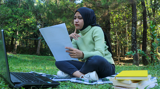 Freelance woman working at natural park, using laptop, reading the document