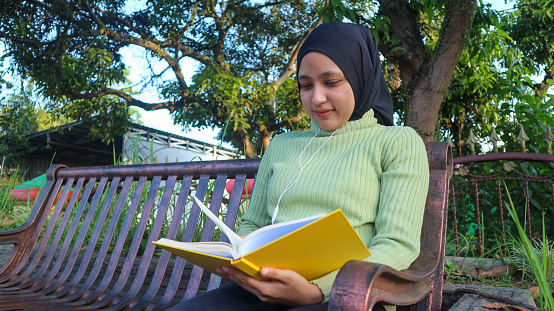 istock Relaxed muslim woman enjoying weekend at park, sitting on bench and reading book, empty space 1646592331