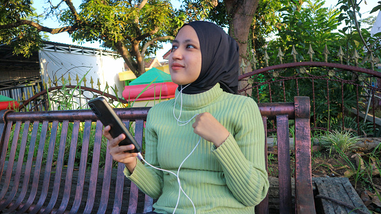 Happy muslim woman listen music on mobile phone at park, using headset, free space