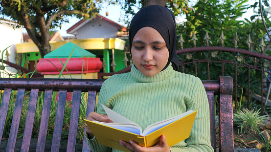 istock Relaxed muslim woman enjoying weekend at park, sitting on bench and reading book, empty space 1646594435