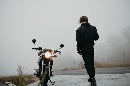 motorcyclist with a motorcycle in the rain and fog in autumn in cold weather.