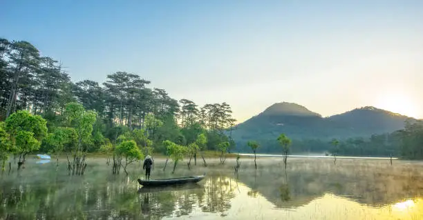 Landscape photo of Da Lat taken from afar, man rowing a boat standing in the middle of Tuyen Lam lake, man rowing a wooden boat on Tuyen Lam lake, beautiful landscape of Da Lat, man rowing a boat in b
