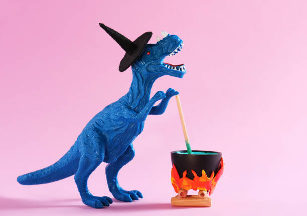 istock Blue dinosaur wearing witch hat is brewing potion in pot on pink background. Halloween greeting card. 1646649698