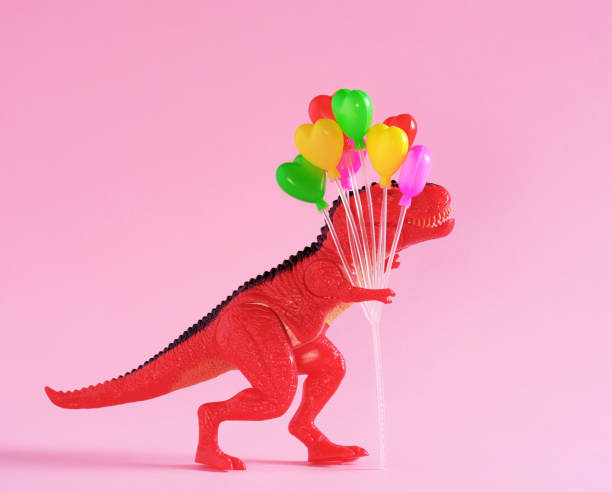 istock Red dinosaur holding colorful balloons on pink background. 1646650245