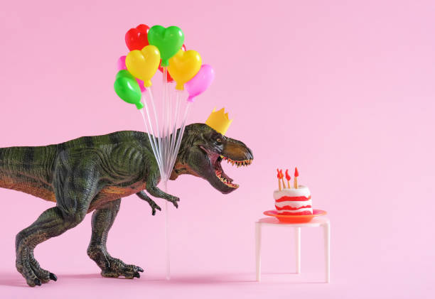 Happy green dinosaur in party crown holding colorful balloons on pink background. stock photo