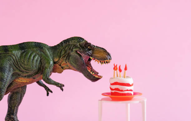 istock Cute dinosaur toy with birthday cake on table on pink background. 1646650267