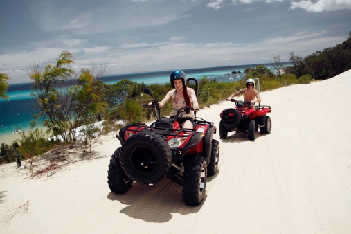 Young male and female driving quad bikes (atv) across a beach on a tropical island.