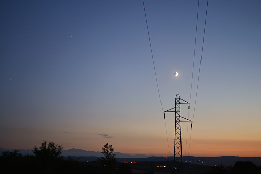 A transmission tower on the background of the Moon and twilight sky