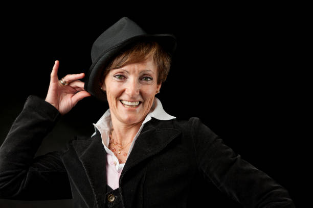 Against a black background, wearing a Borsalino-style hat and a dark jacket, a lady smiles as she does the moves of a 1950s Hollywood dancer.