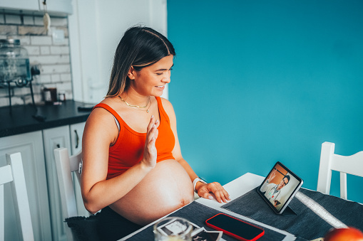 Pregnant woman at home talking on video call with her doctor