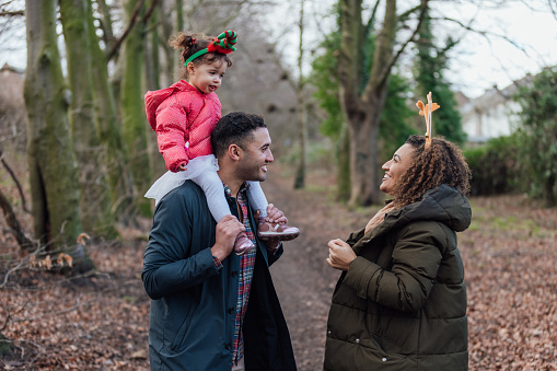A man, his young girl and his sister enjoying a walk in a woodland area during Christmas time in Gateshead, North East England. He is carrying his daughter on his shoulders while standing opposite to his sister while they all talk and bond with each other.