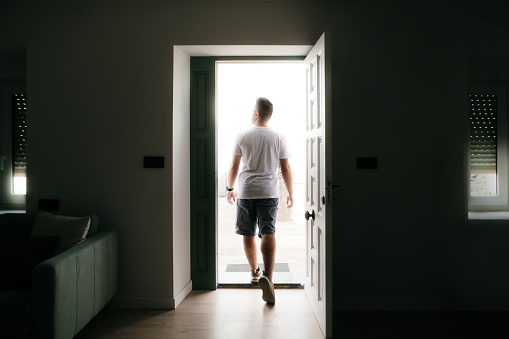 Rear view of a young man walking out the door of the house