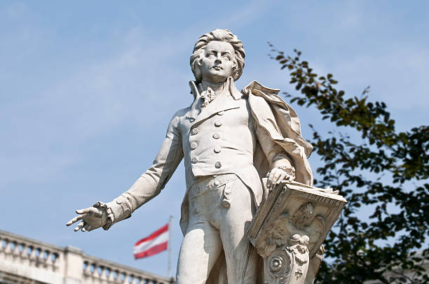Statue of Wolfgang Amadeus Mozart, located in the Burggarten in Vienna. Statue of Wolfgang Amadeus Mozart, located in the Burggarten in Vienna. In the background the Austrian flag on the Austrian National Library. Selective Focus wolfgang amadeus mozart photos stock pictures, royalty-free photos & images