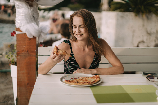 Portrait of a beautiful young woman eating pizza in a restaurant at the seaside during her summer vacation