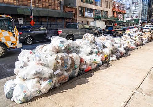 Traffic passing hundreds of bags of garbage, arranged ready for collection from the curb of a street in Midtown Manhattan, New York City.