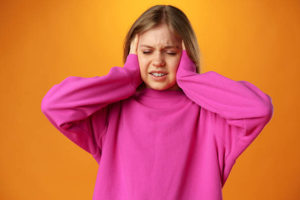 Teenage girl is touching her temples suffering headache on yellow background stock photo