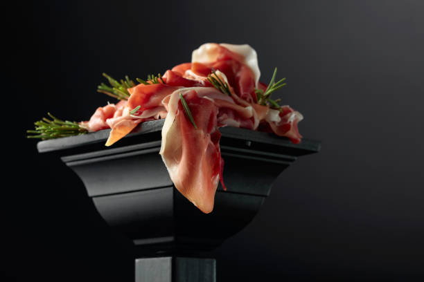 Prosciutto with rosemary on a black podium.