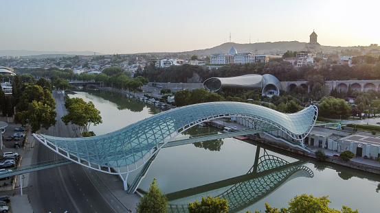 Amazing drone point of Sunrise in Georgian capital -Tbilisi ,  fantastic pedestrian bridge of  Peace over Kura river and  cityscape with President building   (in distance) in left upper corner and  Rike park