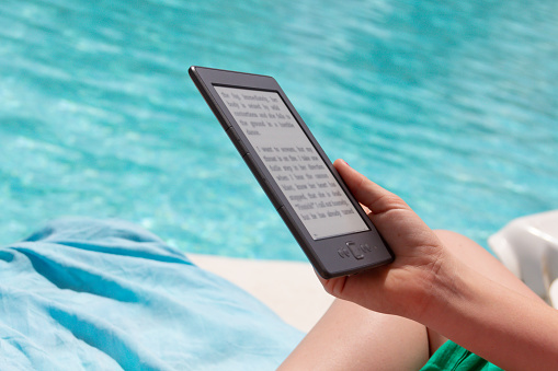 Close up shot of person reading an ebook sitting by swimming pool whilst on vacation in sunny country.