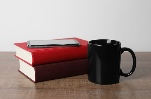 Black ceramic mug, stack of books and smartphone on wooden table