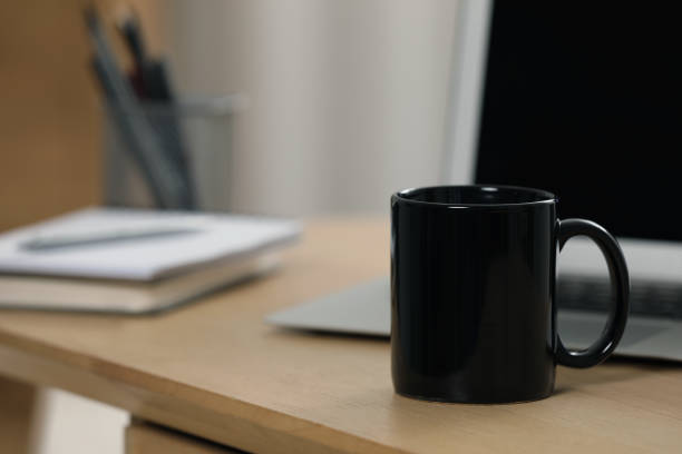 istock Black ceramic mug and laptop on wooden table at workplace. Space for text 1646846564