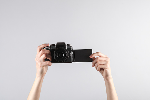 Woman's hand holds a modern digital camera with flip screen on gray background