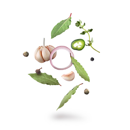 Bay leaves, garlic, onion ring, thyme, black and fresh green peppers falling on white background