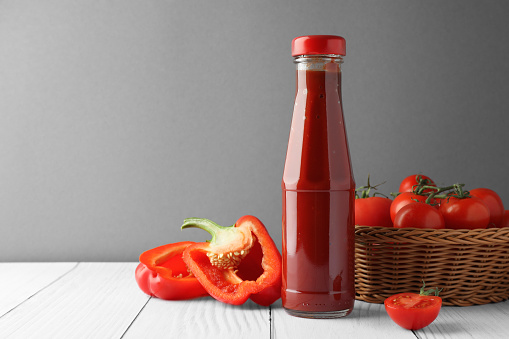 Bottle of tasty ketchup, tomatoes and pepper on white wooden table. Space for text