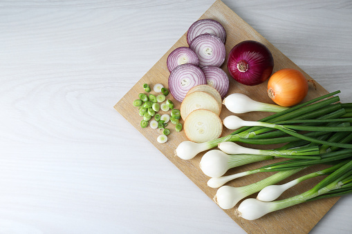 Board with different kinds of onions on white wooden table, top view. Space for text