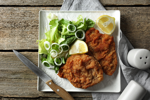 Tasty schnitzels served with lemon and salad on wooden table, flat lay