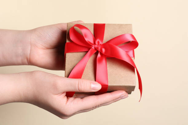 istock Woman holding gift box with red bow on beige background, closeup 1646887791