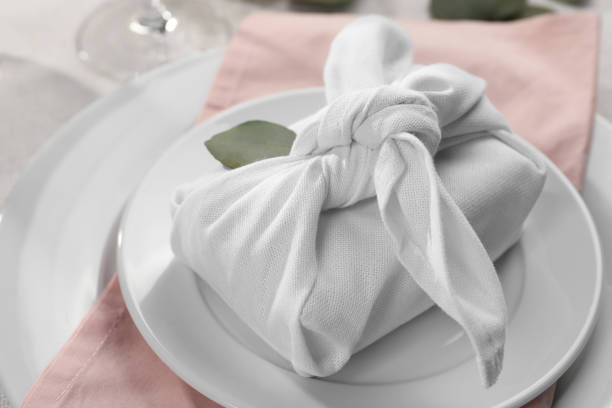 istock Furoshiki technique. Gift packed in white fabric and eucalyptus leaf on table, closeup 1646887816