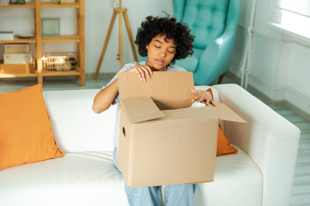 African girl unpacking delivery looking in box. Happy woman opening carton box. Female getting parcel looking at delivered goods items. Satisfied client positive feedback quick express deliver chica africana desempacando la entrega buscando en caja. mujer feliz abriendo caja de cartón. mujer recibiendo paquete mirando los artículos de mercancías entregados. satisfacción del cliente retroalimentación positiva entrega rápida exprés.