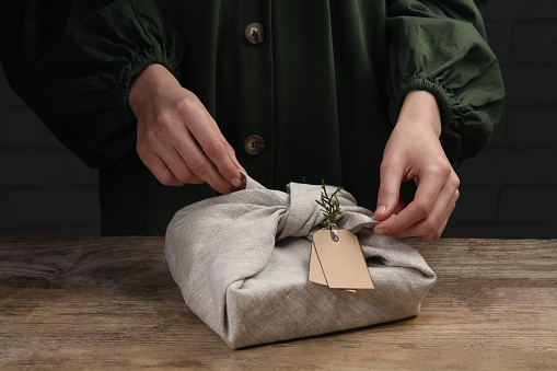 Furoshiki technique. Woman wrapping gift in fabric at wooden table, closeup