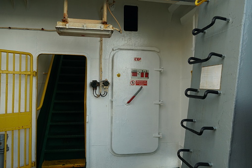 Paranagua, Brazil, 04 16 2023, White metal door with stickers is closing the entrance to CO2 room on the container vessel. The wall in aft station of the ship are partly rusted has white colour.