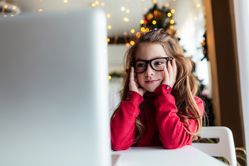 Girl sitting on a table and using laptop in front of Christmas tree