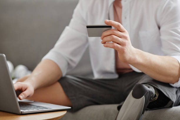 istock Man with prosthetic leg entering credit card information online using laptop 1646904055