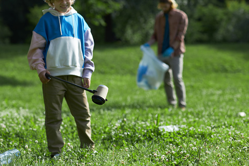 Closeup of little boy picking up trash in nature eco activist family, copy space