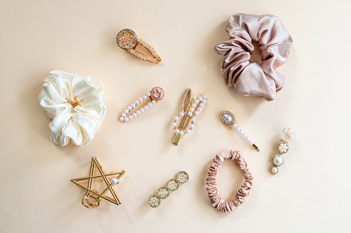 Collection of trendy silk elastic band scrunchies and pearl hair clips on color background. Diy accessories and hairstyles concept, luxury color