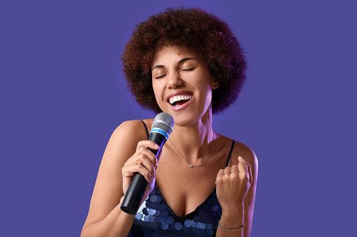 Curly young woman with microphone singing on purple background