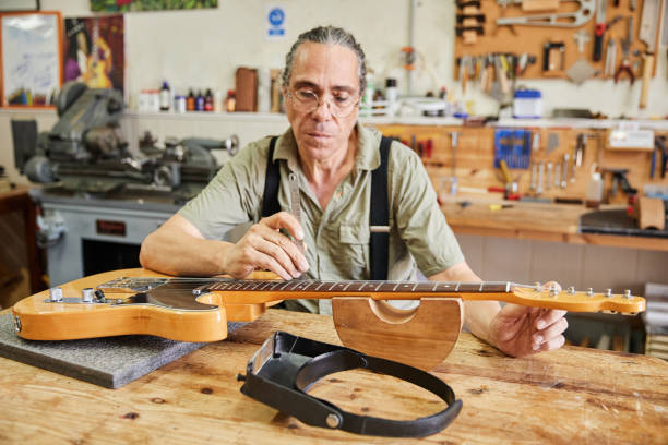 Middle-aged luthier fixing the strings of a guitar in his workshop.