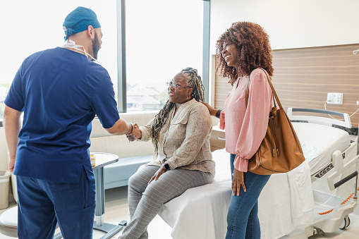 The mid adult daughter supports her mature adult mother when the male surgeon comes into the hospital room to greet her.