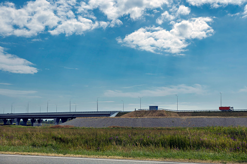 Side view of a cargo truck moving along a highway. Road bridge with passing traffic