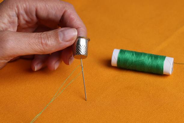 istock Woman sewing on orange fabric with thimble and needle, closeup 1647052076